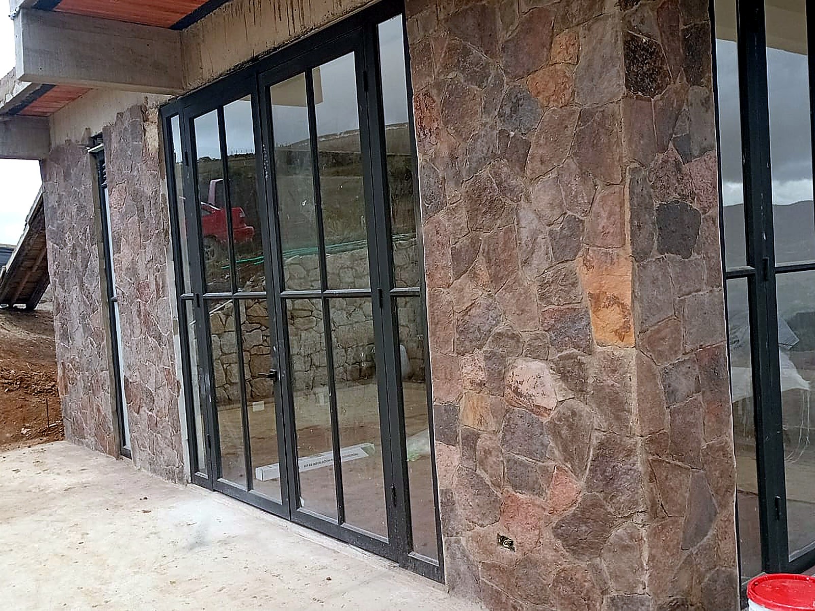 Fachada lateral en piedra con carpintería metálica negra y placa en concreto