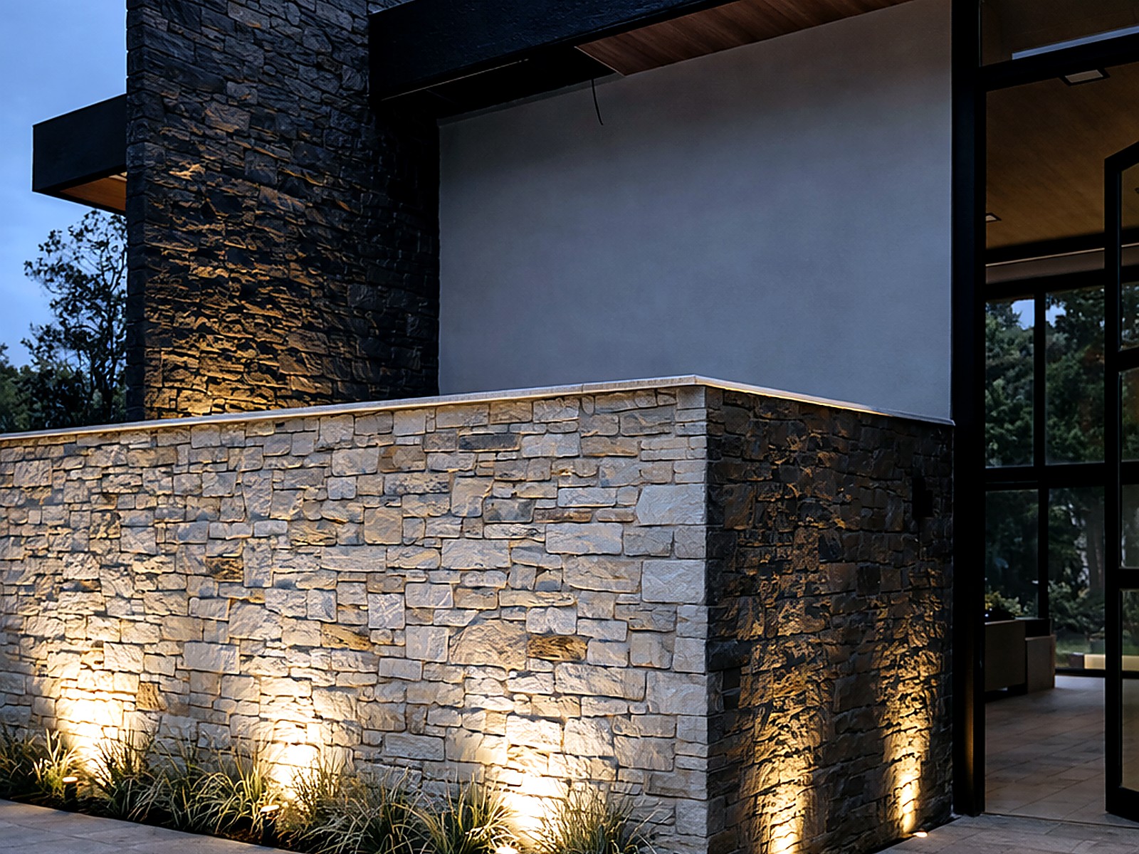 Muro en piedra iluminado al anochecer con alero negro y cielo en madera