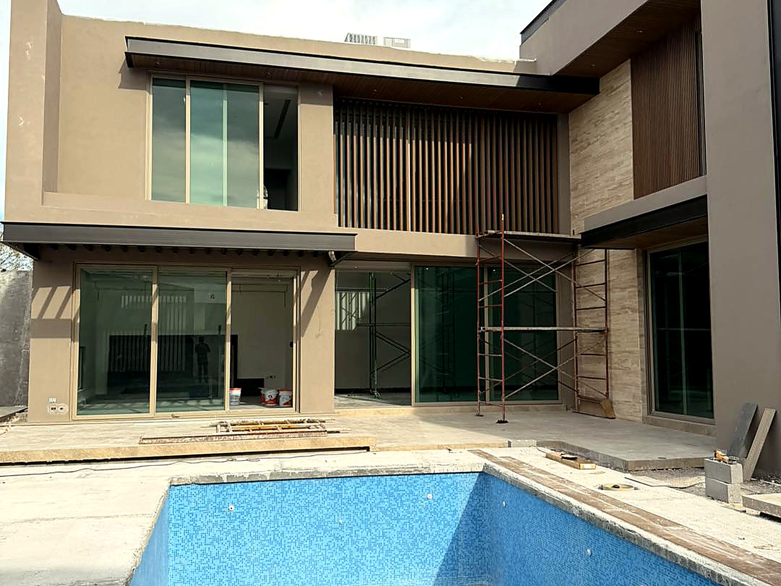 Fachada posterior con piscina, celosías en madera y ventanales corredizos