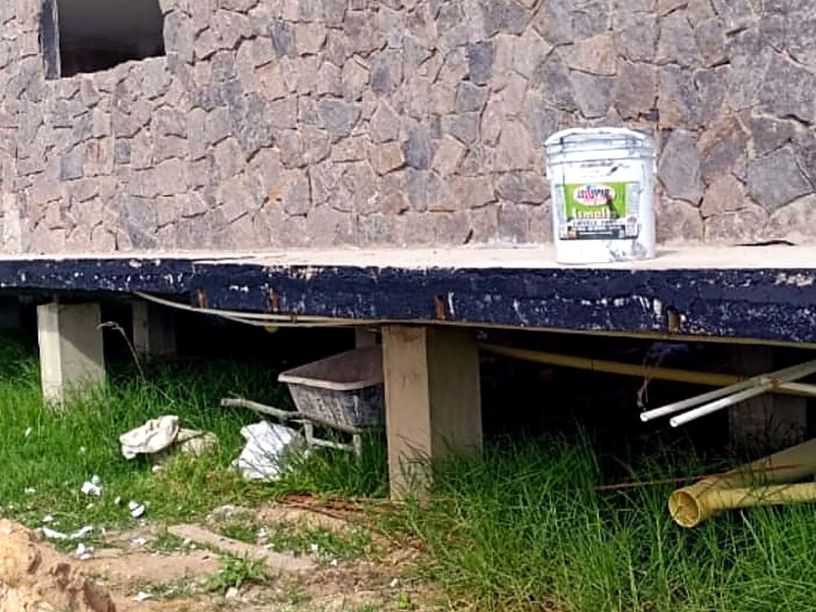 Muro en piedra con alero en madera y cubierta negra sobre la placa elevada