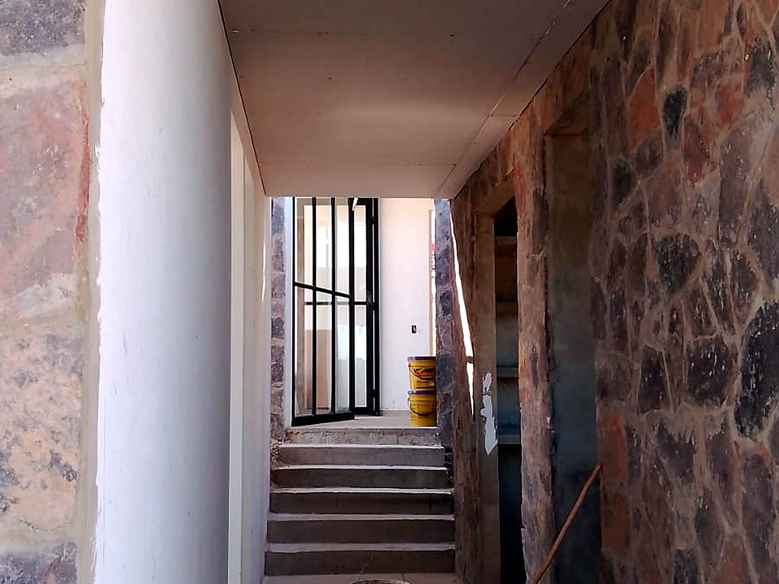 Pasillo interior entre muro en piedra y muro pañetado hacia la escalera