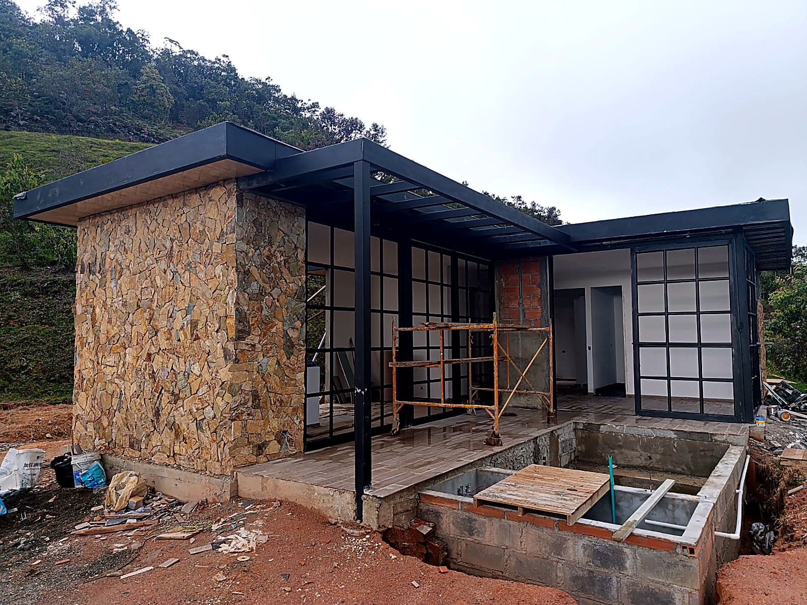 Casa de un piso con muro en piedra, pérgola metálica negra y ventanales cuadriculados
