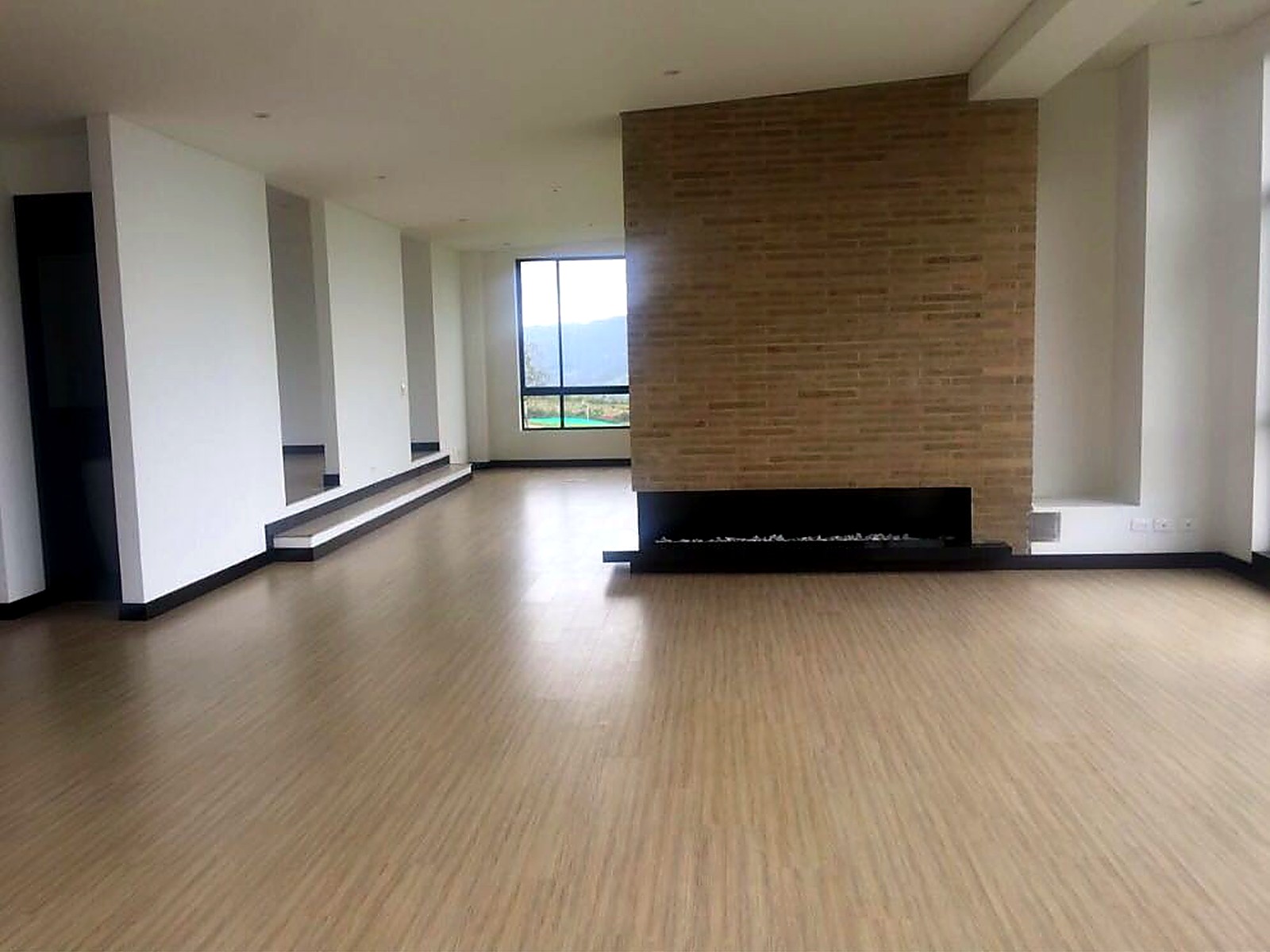 Salón con chimenea lineal en muro de ladrillo y pisos en madera