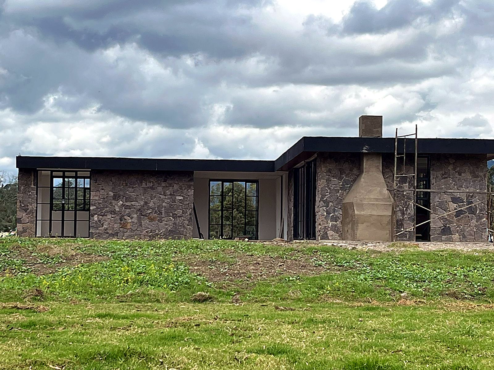 Fachada con ventanales en carpintería negra y chimenea en concreto