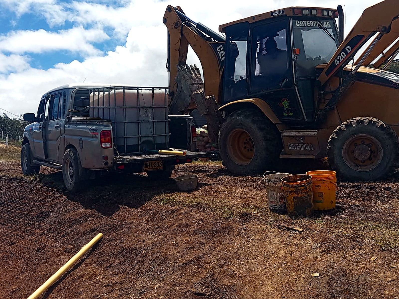 Retroexcavadora y camioneta con tanque de agua en el frente de obra
