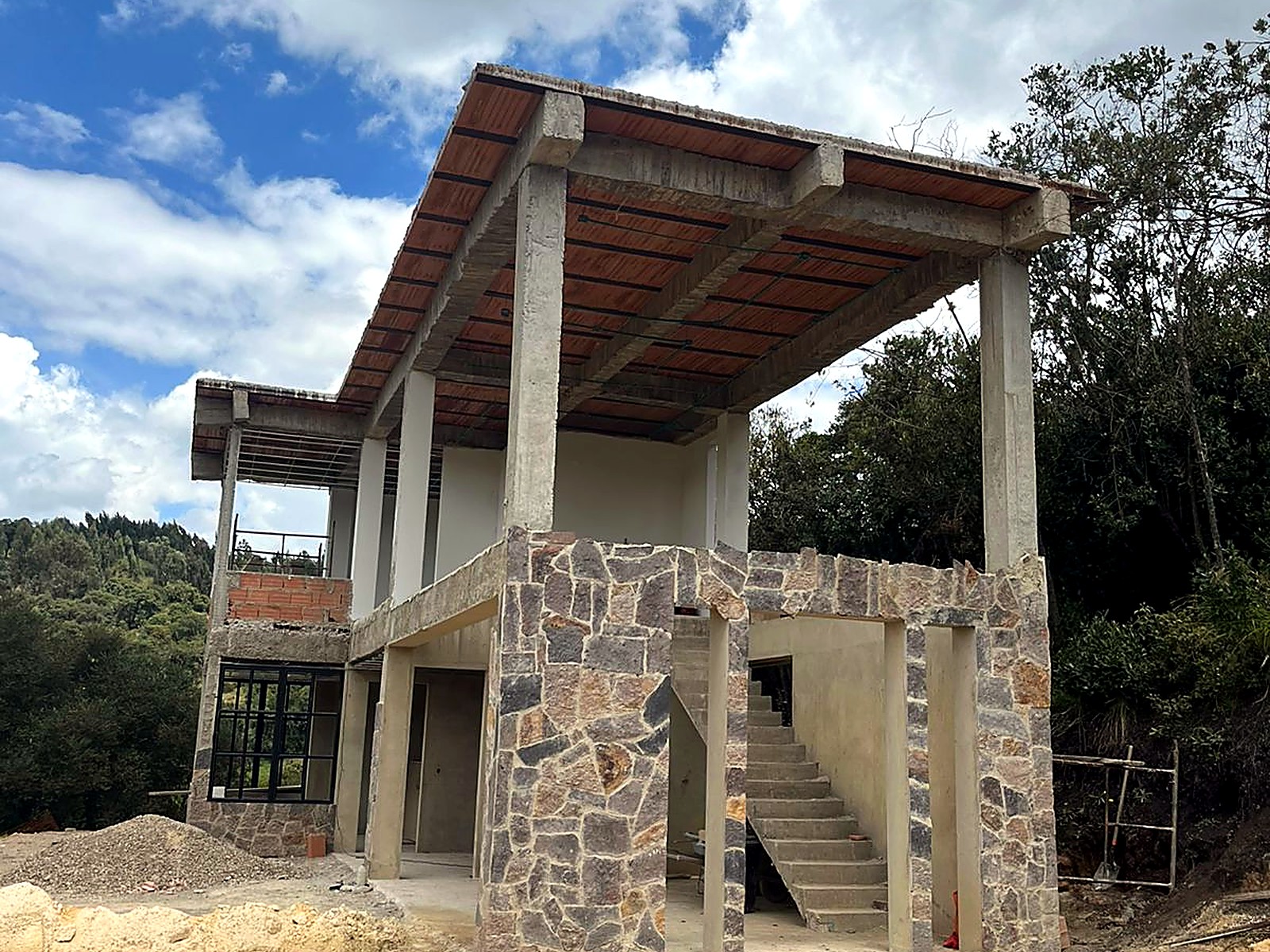 Casa de dos niveles con pórticos en concreto, muros en piedra y losa con formaleta en madera