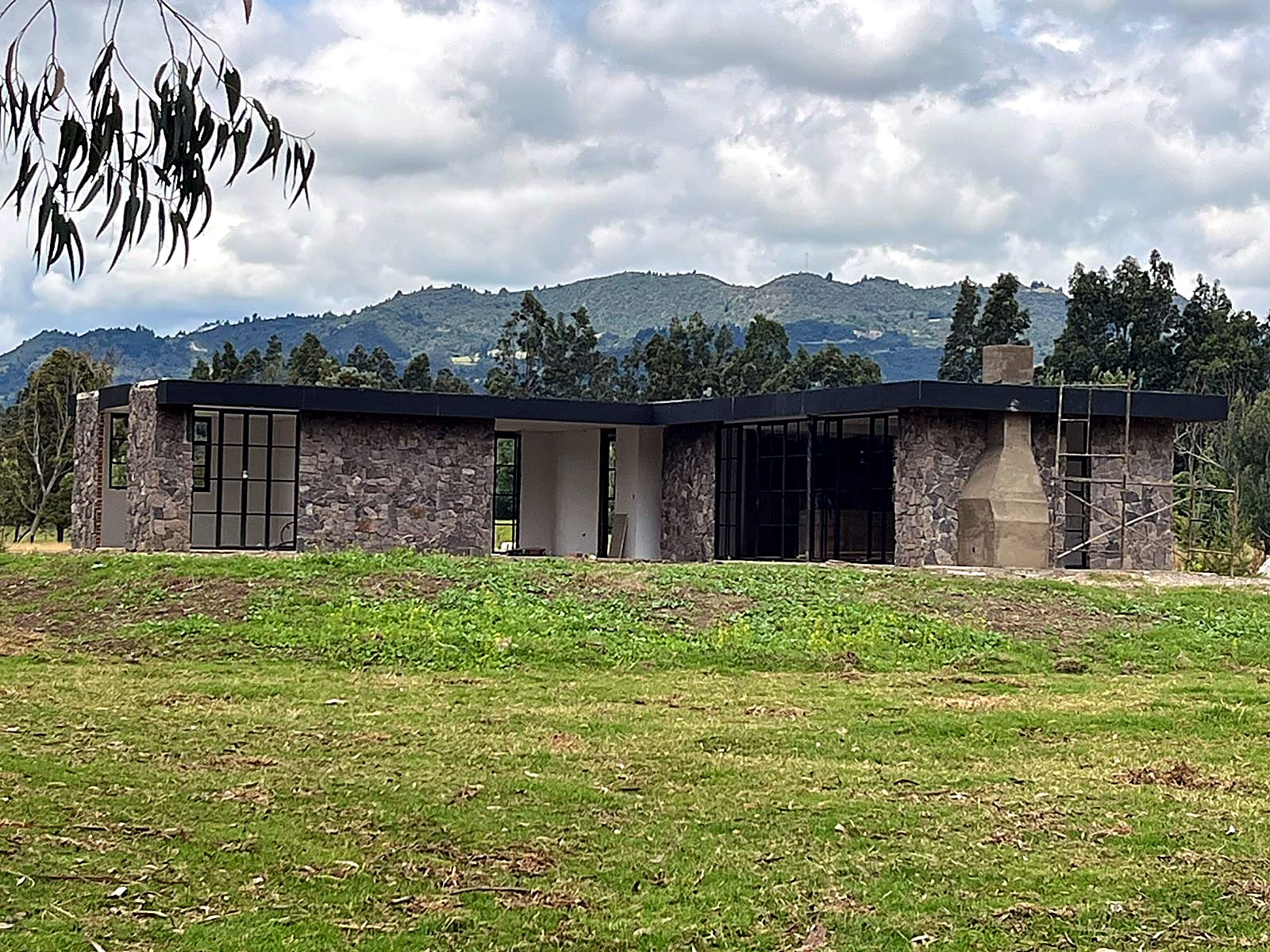 Casa en piedra de un nivel con cubierta plana negra frente a la montaña