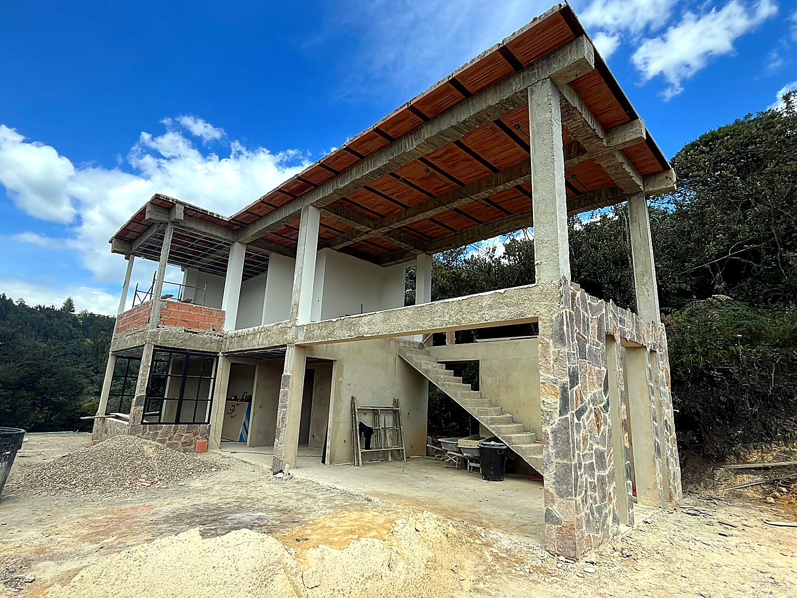 Vista lateral de la casa con voladizo, escalera en concreto y muros en piedra