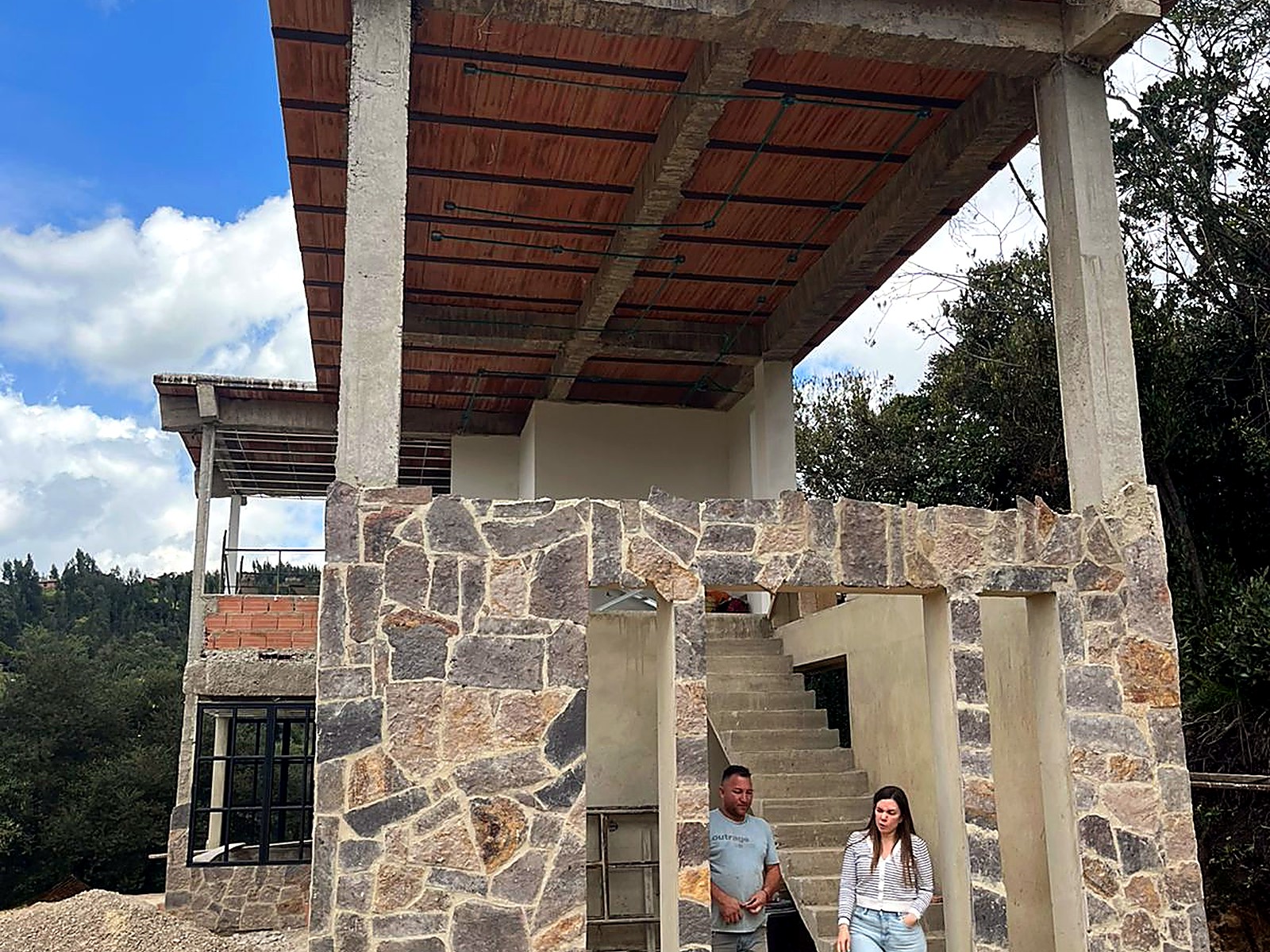 Frente de la casa con muros en piedra y escalera exterior en concreto