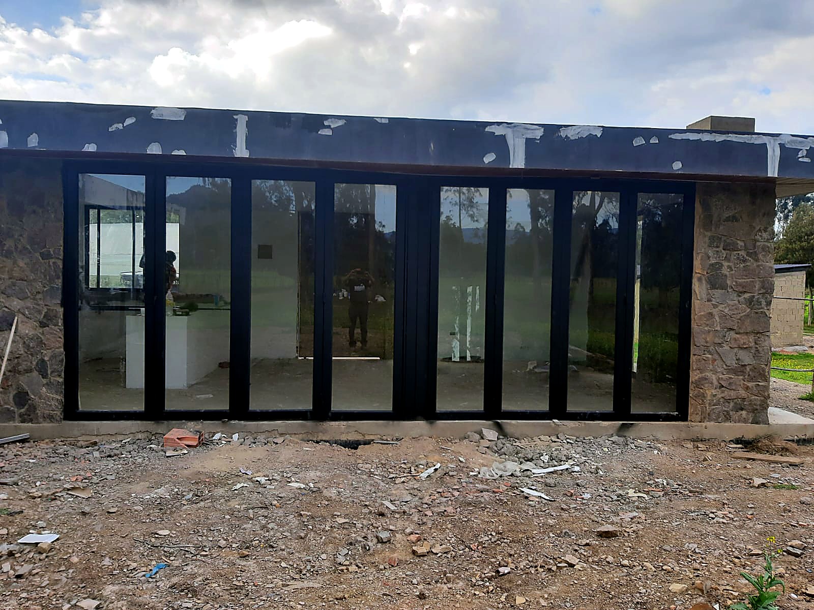 Fachada con ventanal corrido en aluminio negro entre muros de piedra