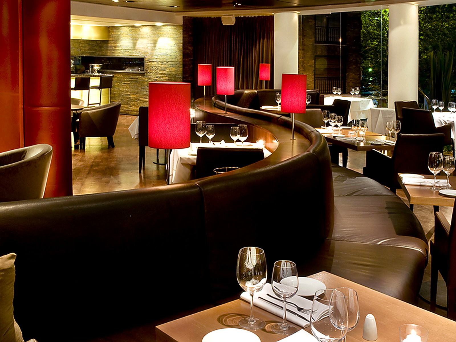 Barra al fondo, sofá curvo y lámparas rojas en el comedor principal