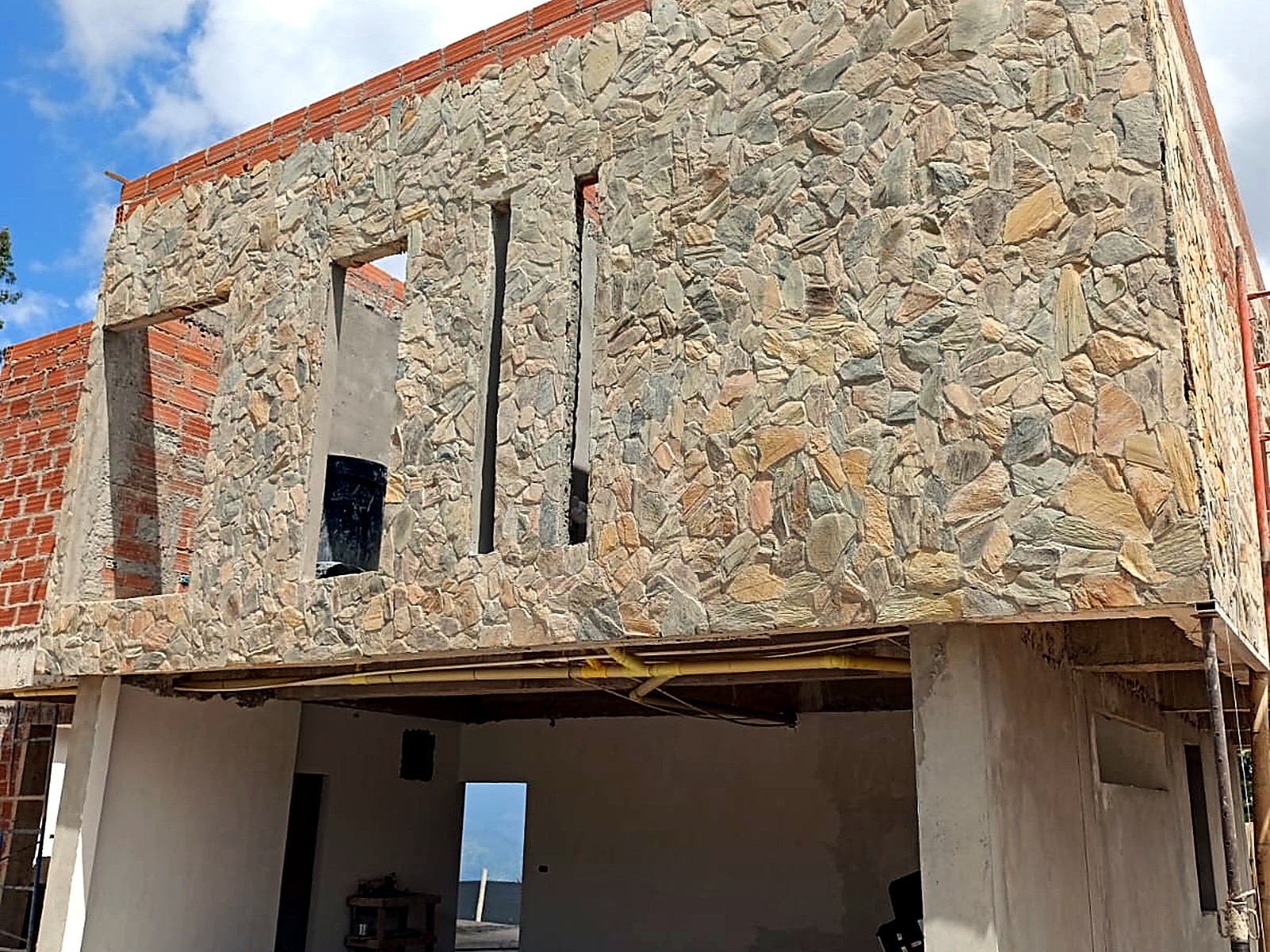 Fachada en piedra con ventanas verticales sobre el nivel en concreto