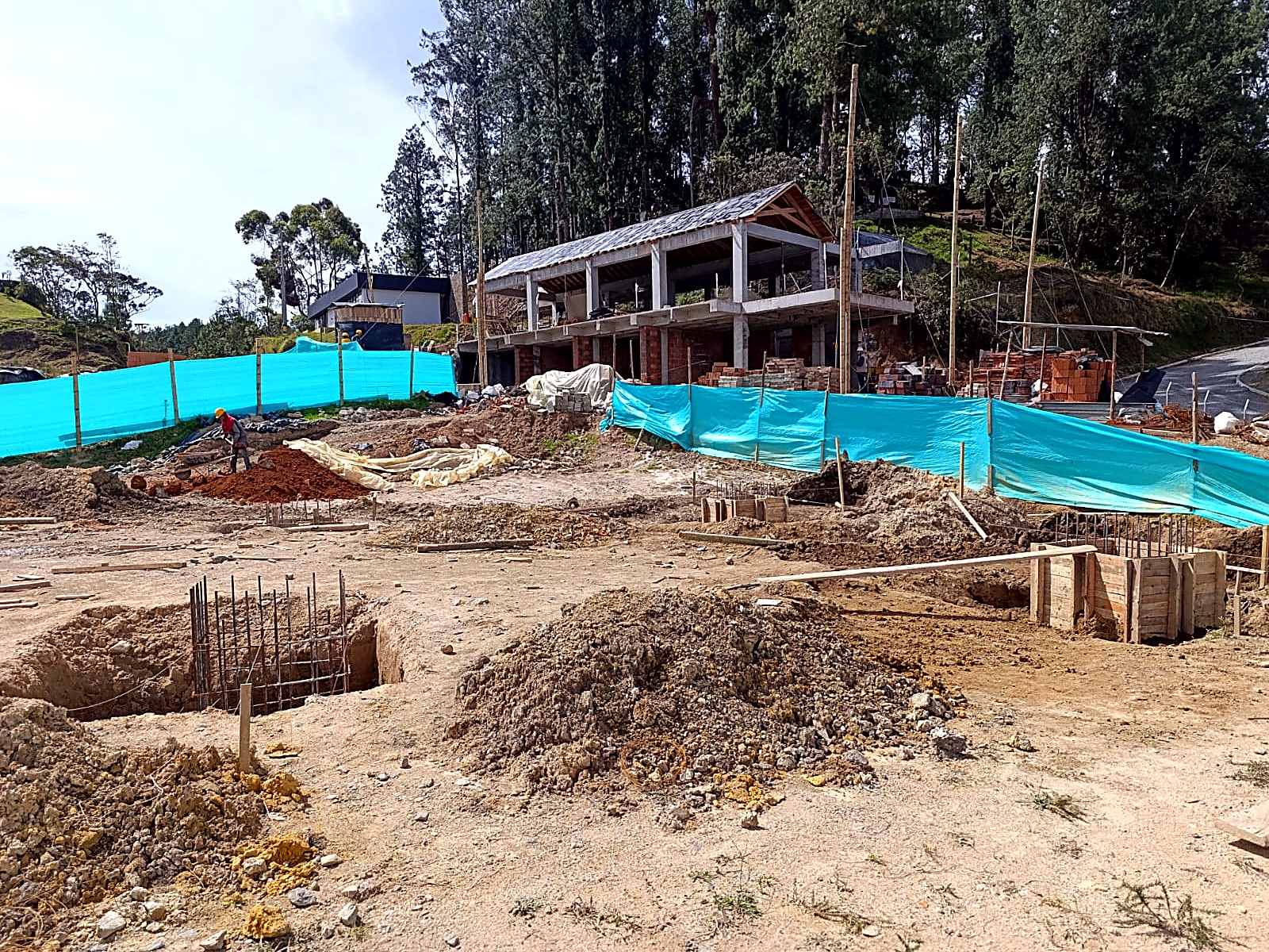 Zapatas excavadas y ferralla en primer plano con la obra al fondo