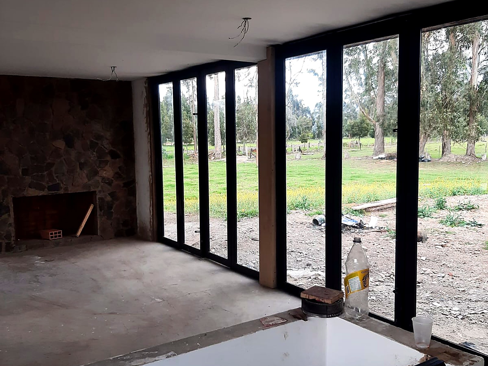 Interior con chimenea en piedra y ventanal hacia el potrero